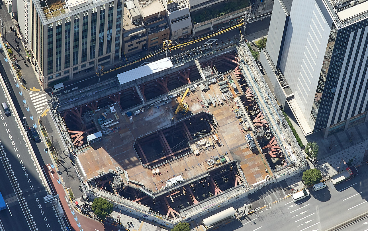 The underground construction progresses by installing a temporary deck and feeding materials from above.